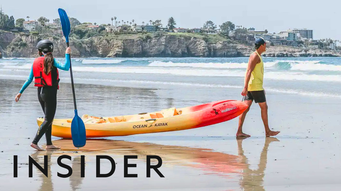 Photo of two people carrying a Kayak on the beach in La Jolla, California. They are walking towards the ocean.