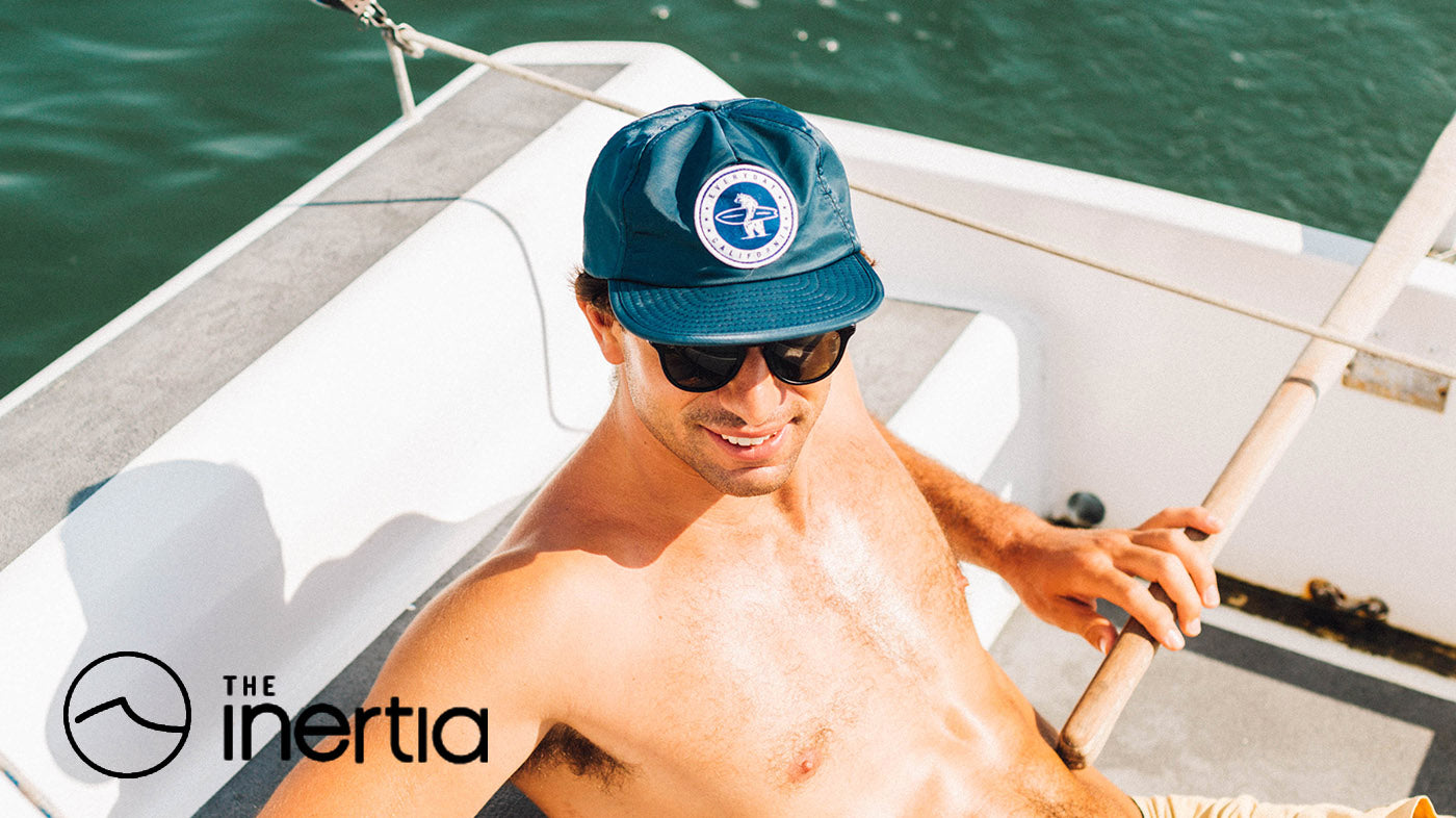 Photo of a man wearing a navy colored waterproof snapback hat, sitting in a boat in the water