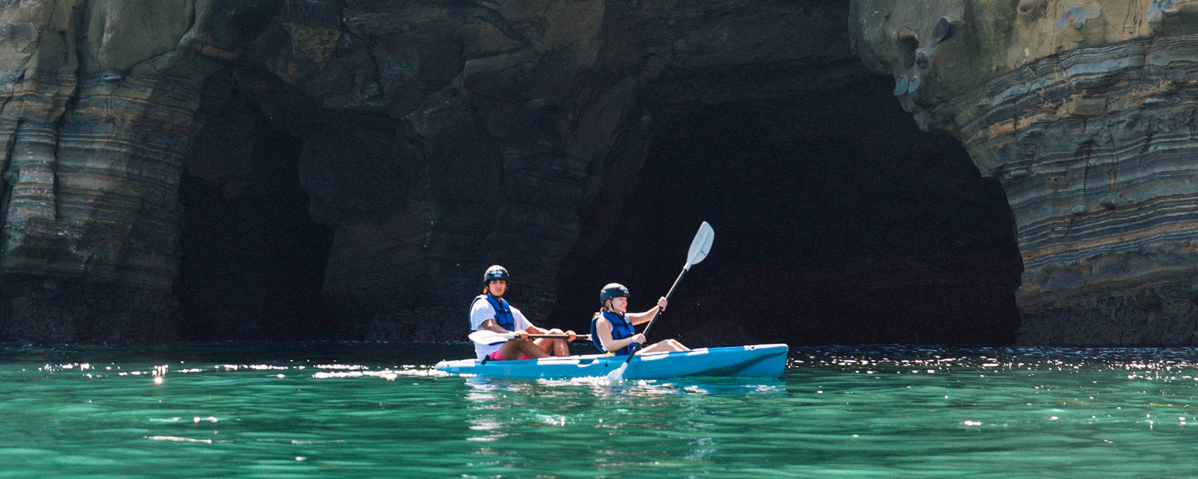 Two kayakers on a Kayaking Tour with Everyday California, paddling their kayak in front of the mouth of a sea cave in La Jolla.