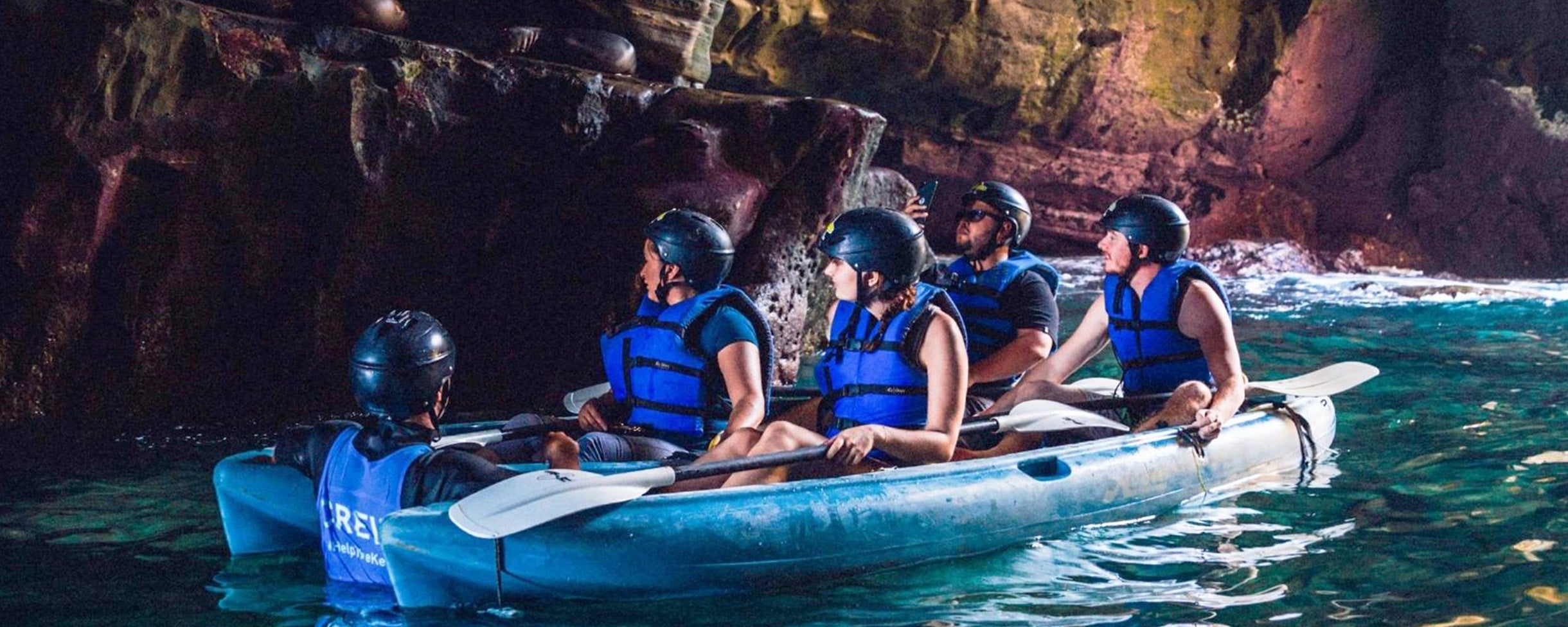 A group of 4 kayakers sitting on their kayaks inside of one of the Seven Sea Caves, learning about the history of La Jolla from their Everyday California tour guide who sits nearby in the water.